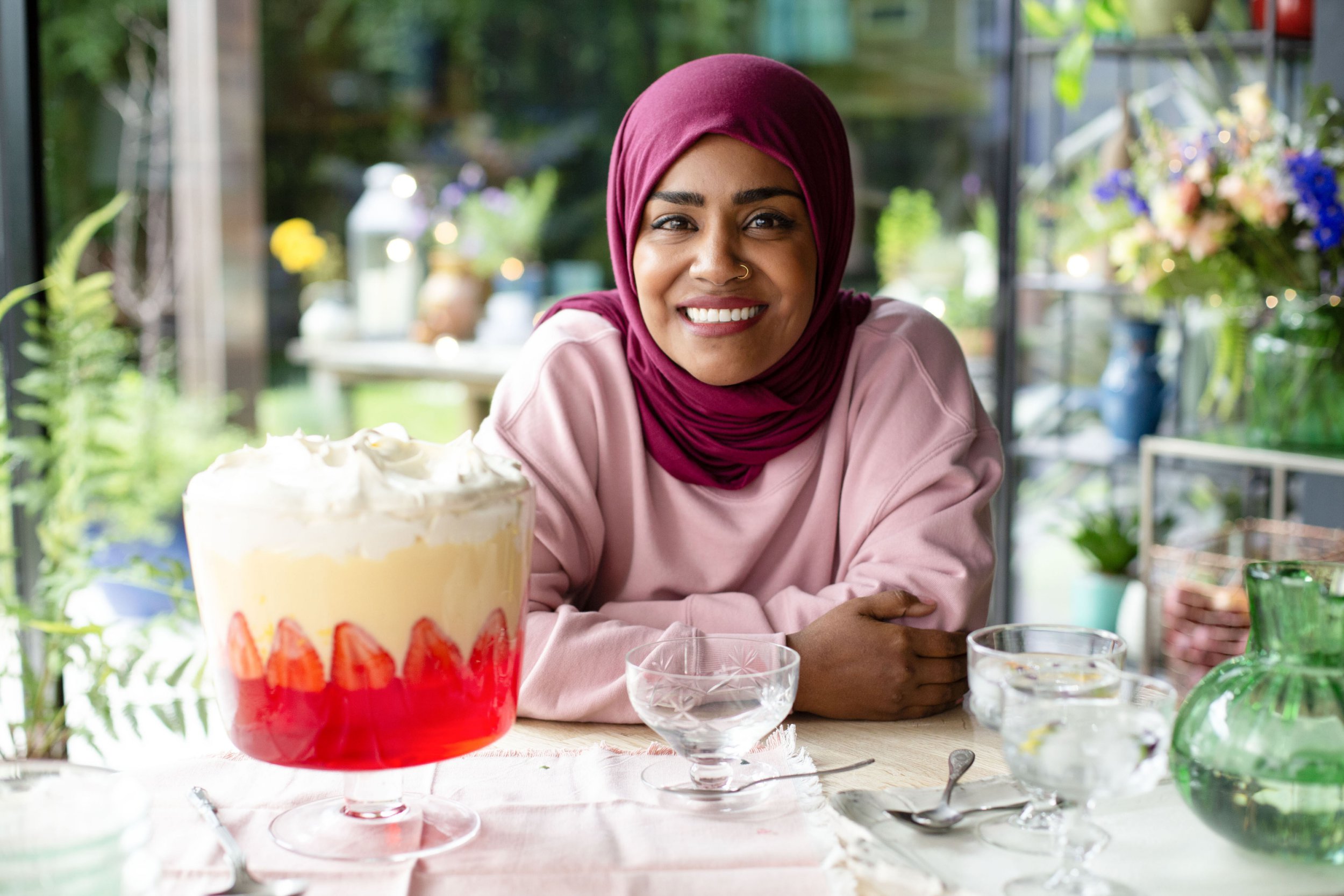 Bake Off winner Nadiya Hussain smiling next to a trifle on BBC show Nadiya's Cook Once, Eat Twice