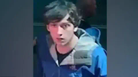 Lancashire Constabulary A CCTV shot of Thomas Dures, 21, who is wearing a blue coat and a black t-shirt and has medium-length dark hair